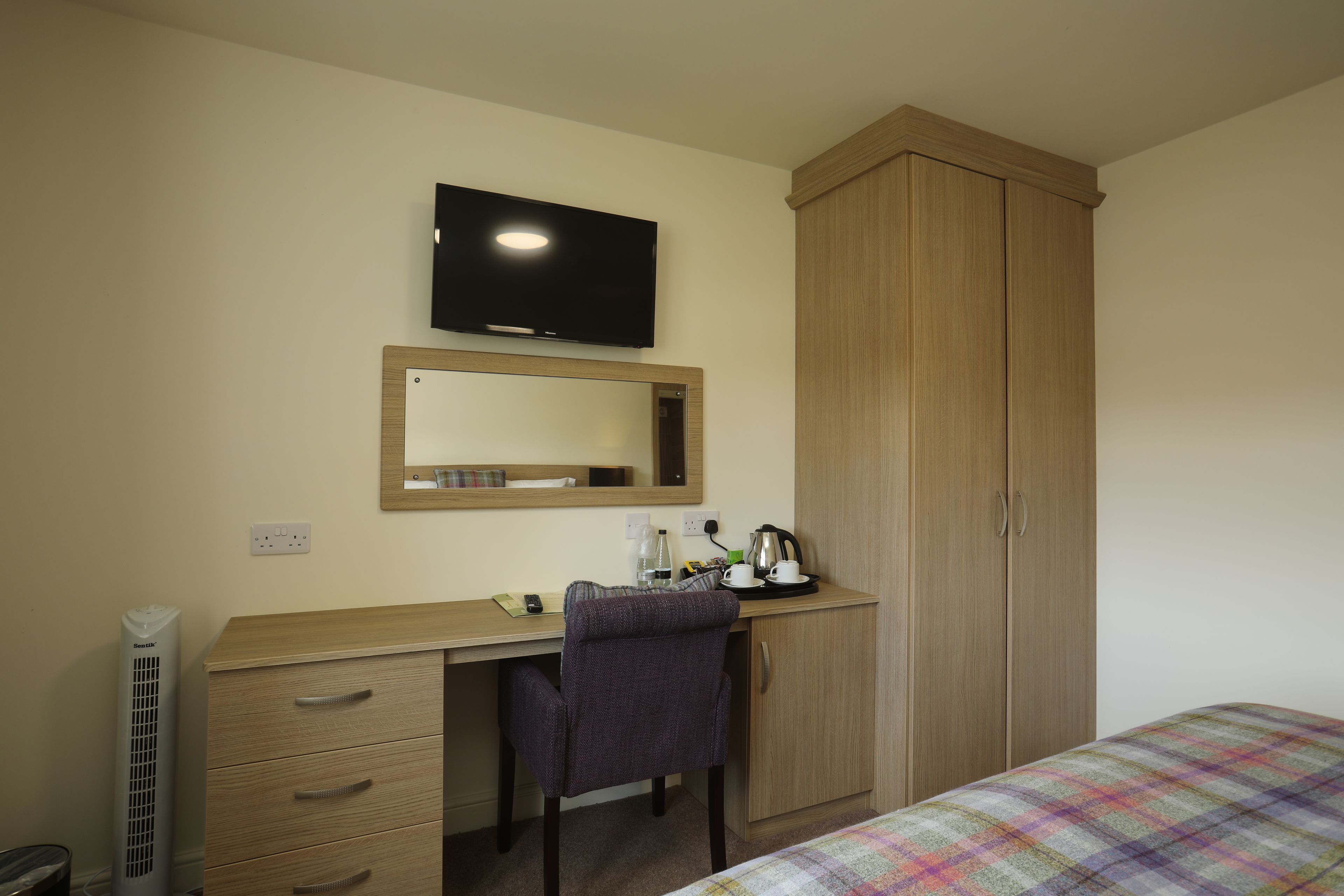 A bedroom with a bed, a desk with a chair, a wardrobe, a television, and a heater.