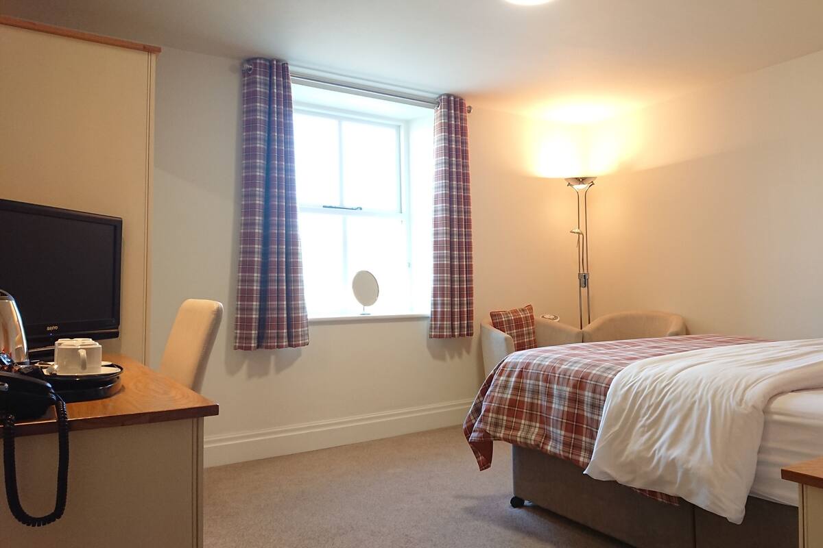 A hotel room with a bed, a desk with a telephone, a lamp, and a television.