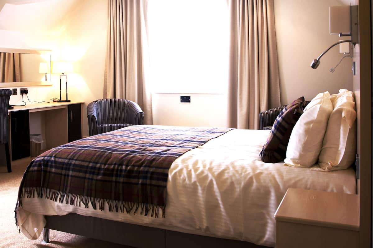 A hotel room with a bed, a desk, a chair, and a window with curtains.