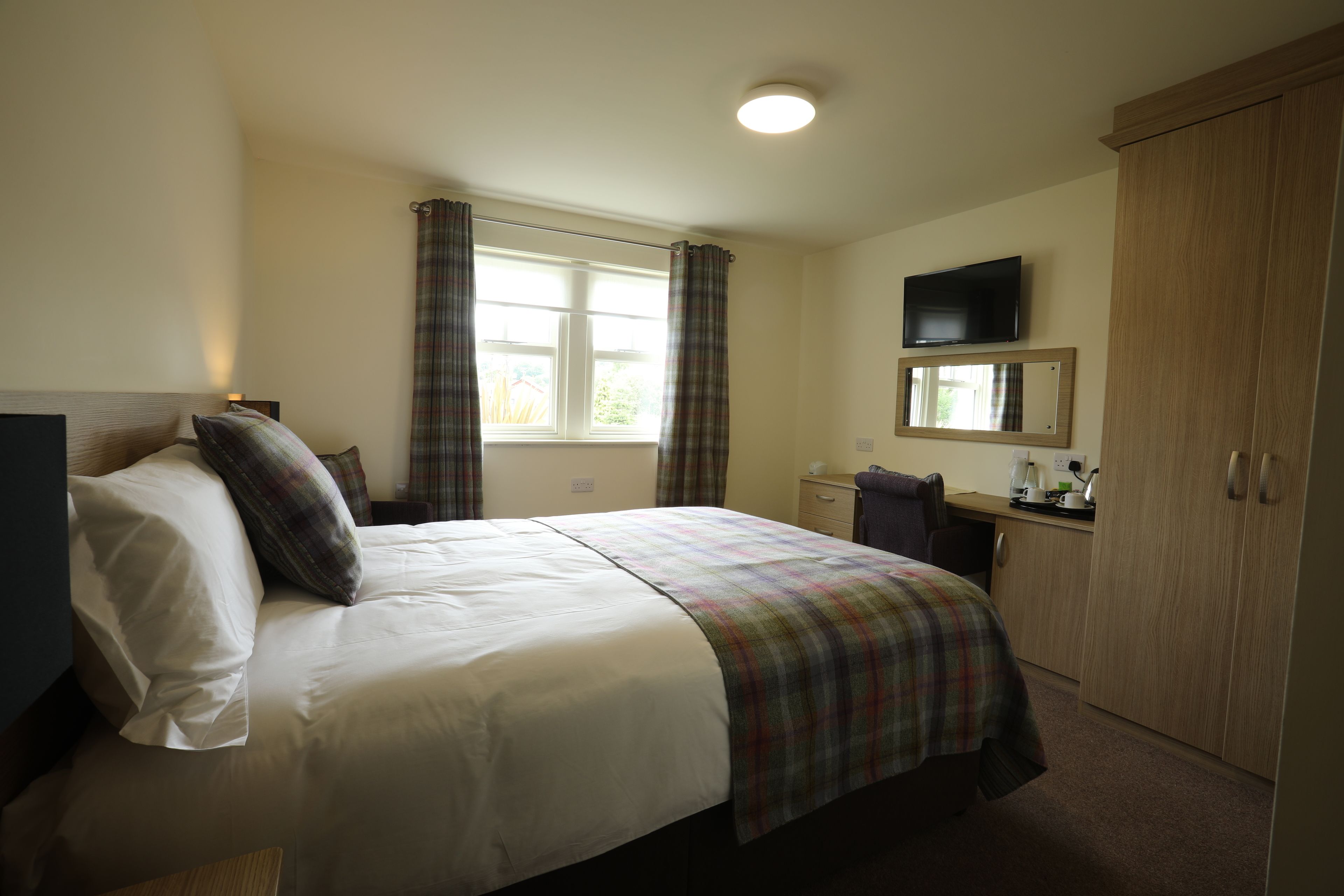 A hotel room with a bed, a desk, a television, and a wardrobe.