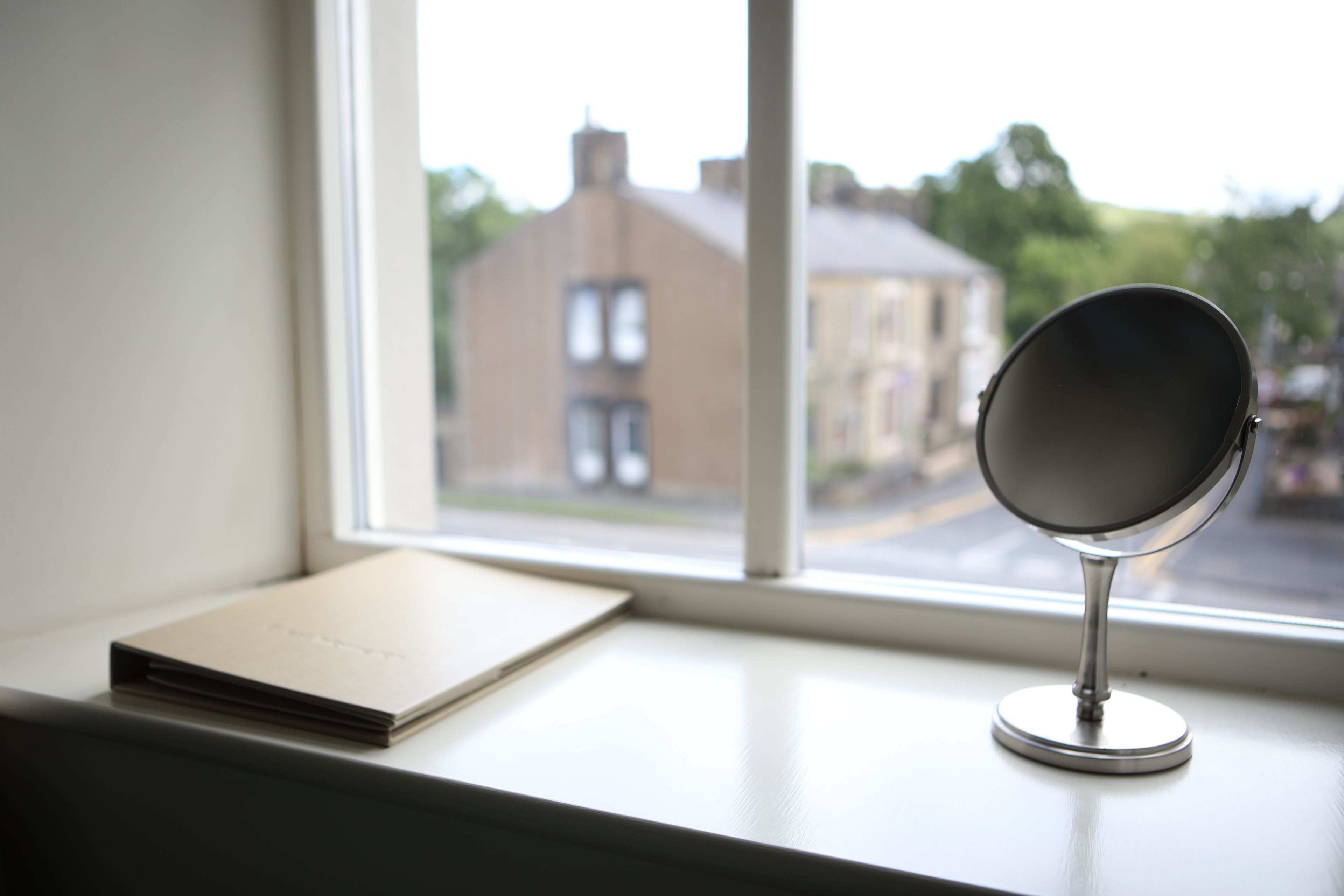 A mirror on a windowsill with a view of a building outside.