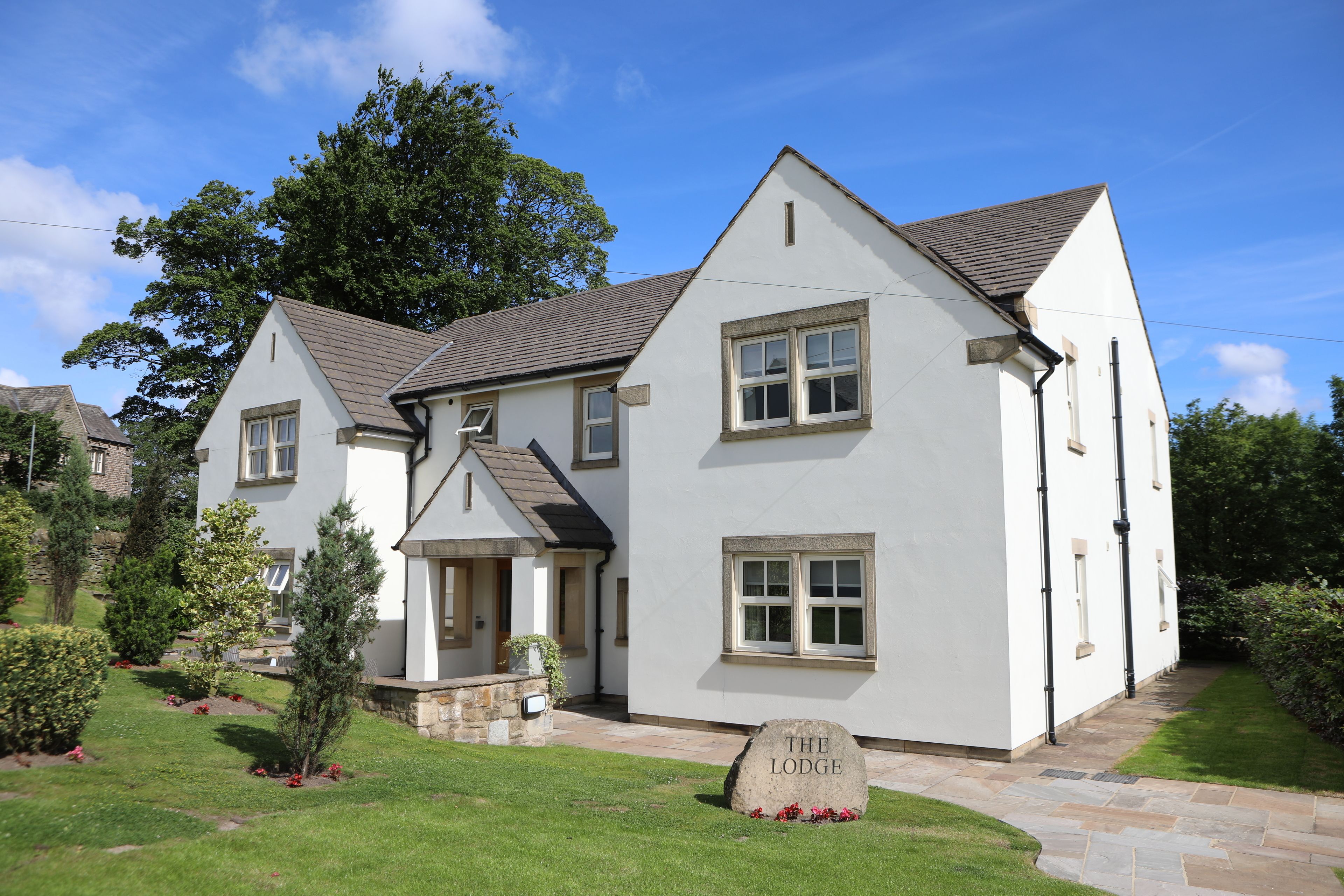 A two-story white building with a stone pathway leading to the entrance, surrounded by greenery and a clear sky.