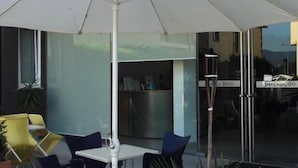 Zona de estar al aire libre con una sombrilla blanca, un mostrador de recepción y un puerta de cristal.