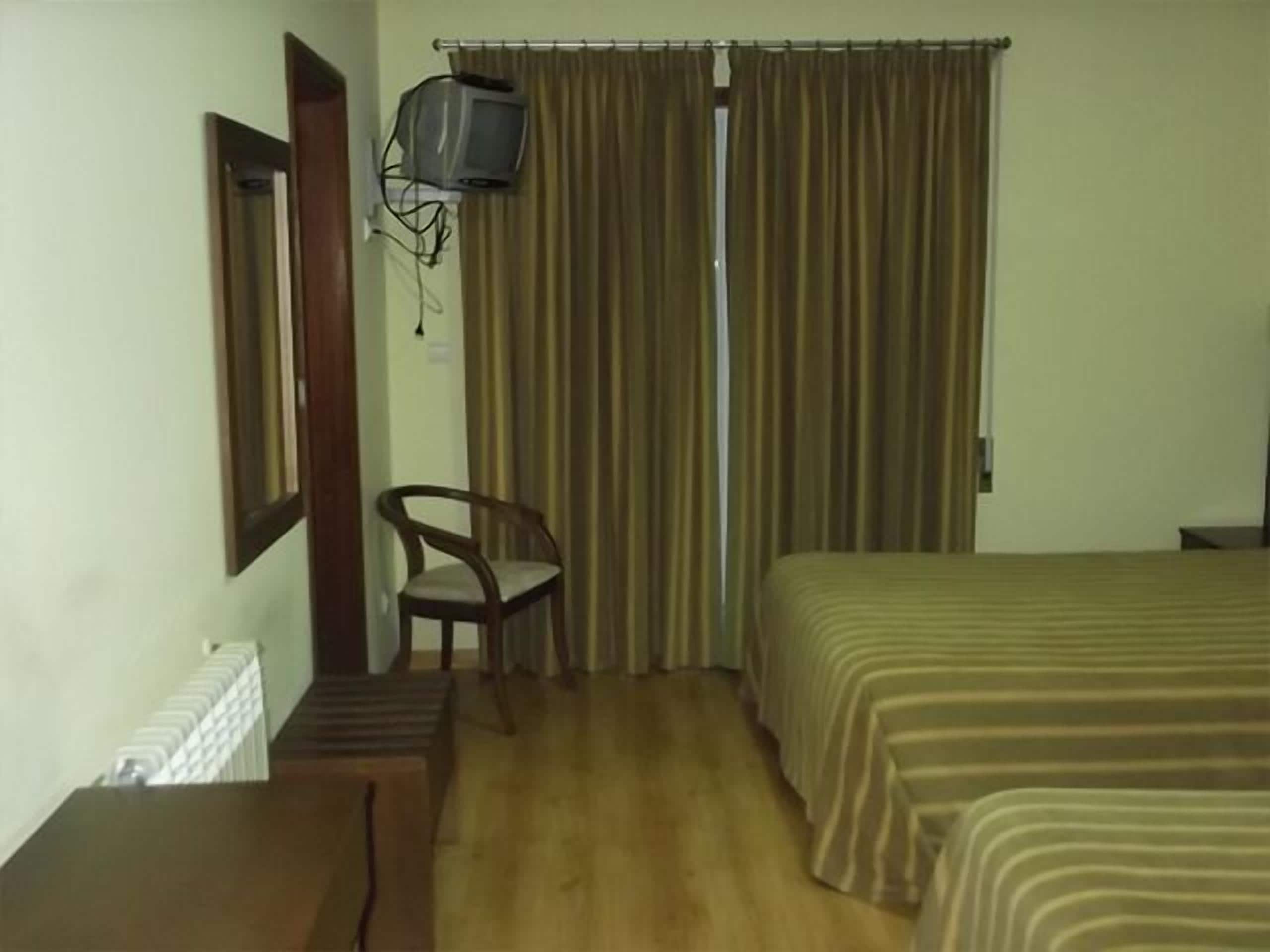 A room with a bed, a chair, a television mounted on the wall, and a window with curtains.