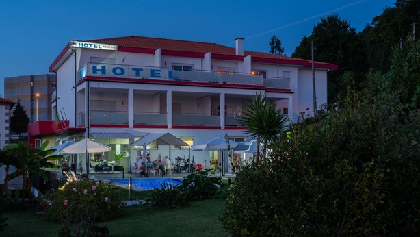 Un hotel con piscina, mobiliario exterior y techo rojo.