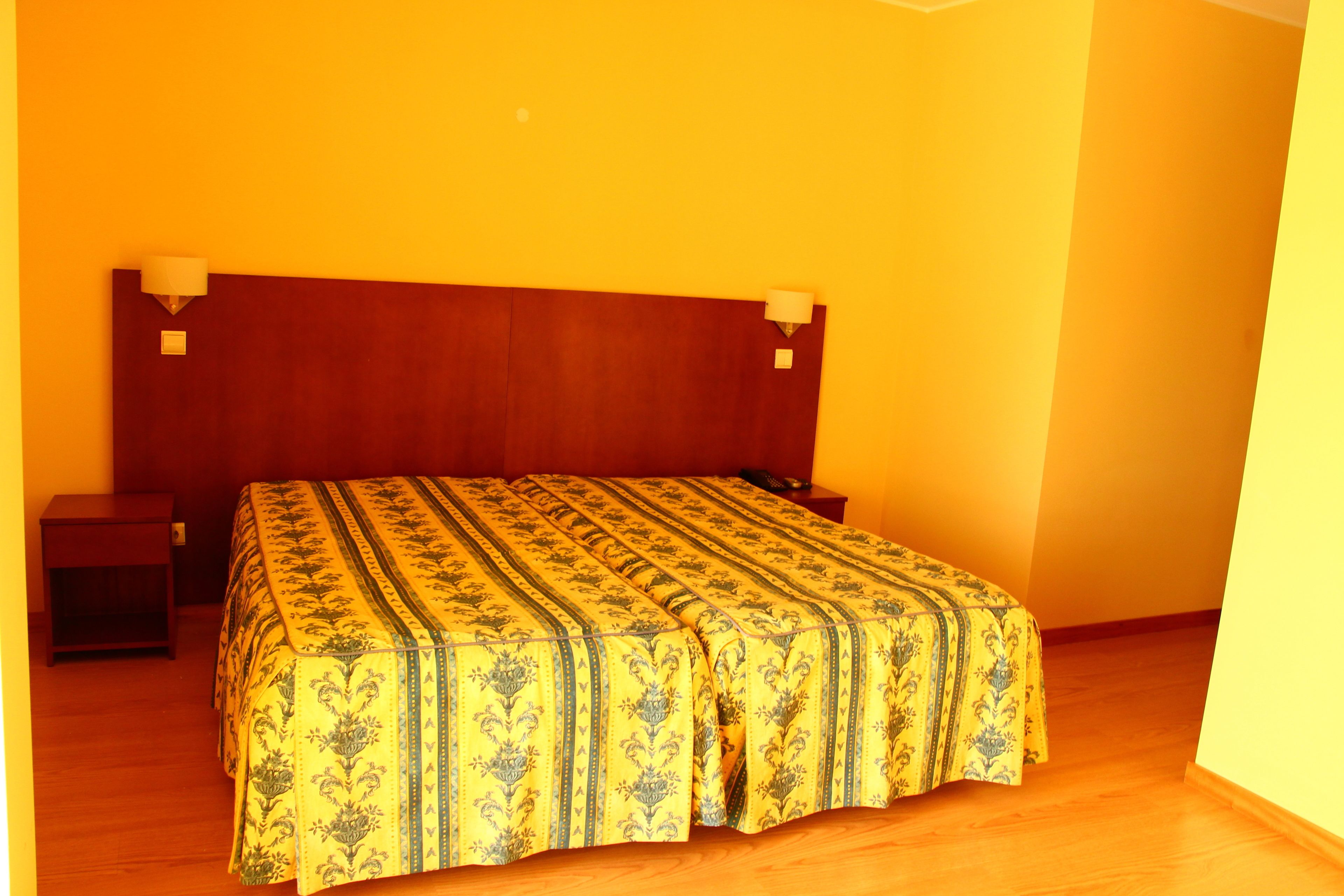 A bedroom with a wooden headboard, a patterned bedspread, two bedside tables, and a nightstand.