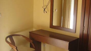 Una habitación pequeña con un escritorio de madera, una silla y un espejo.