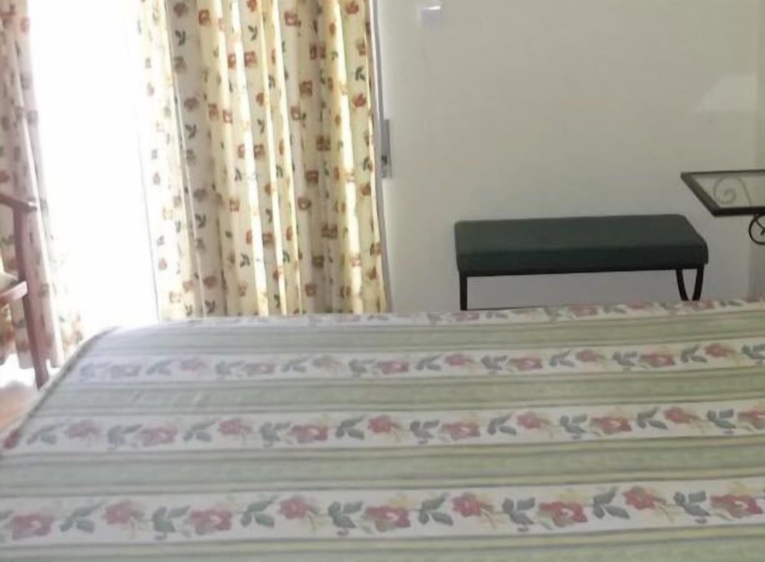 Una stanza con un letto, una panca e una TV a parete.