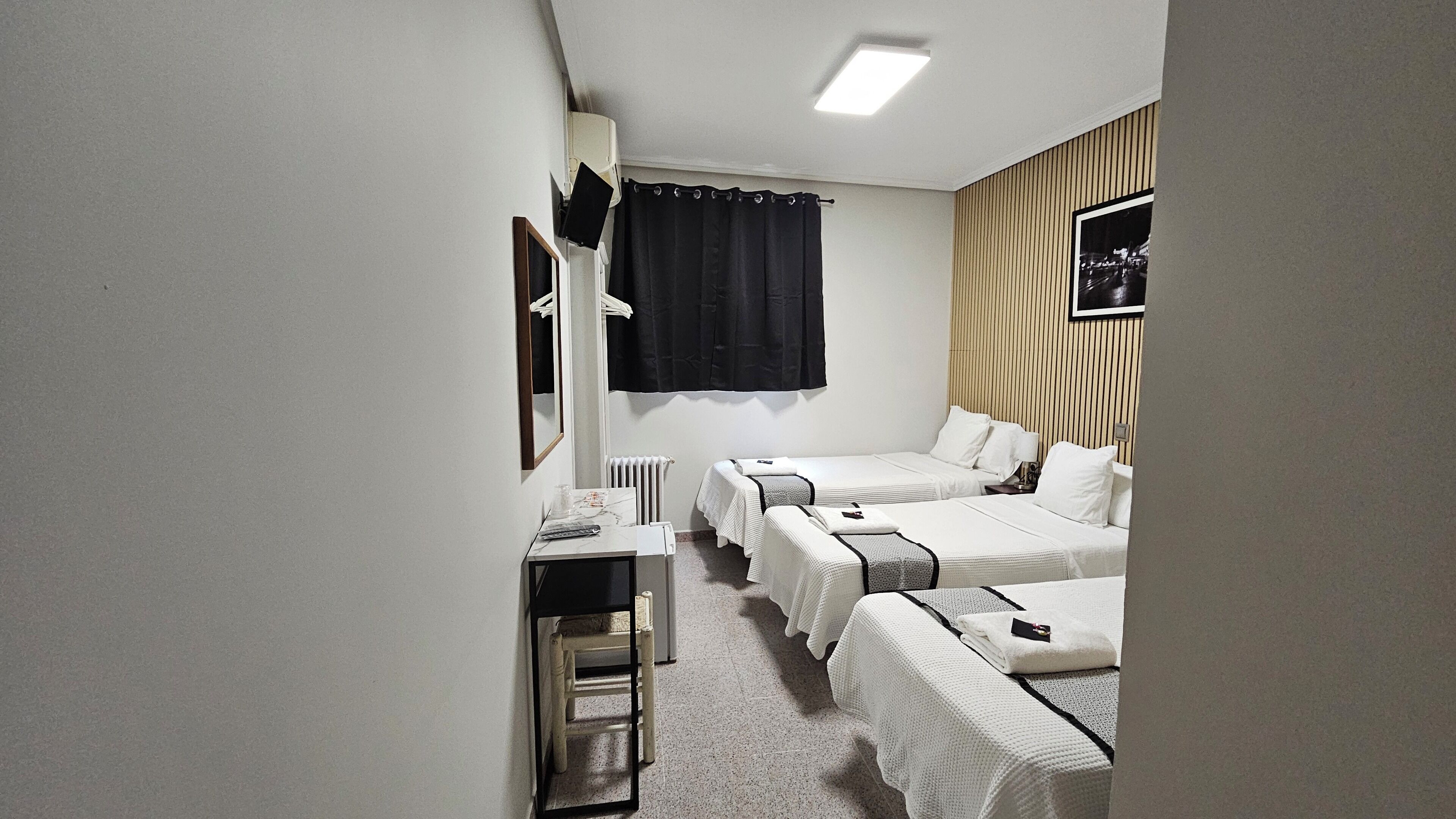 A hotel room with two beds, a desk, a chair, a radiator, and a framed picture on the wall.