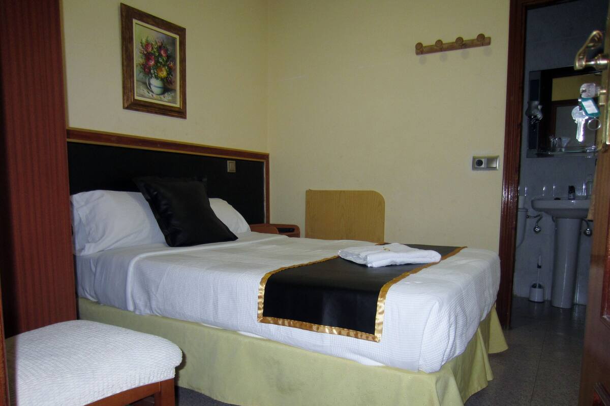 A hotel room with a bed, a chair, a painting, and a bathroom visible through an open door.