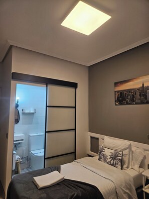 Habitación de hotel con una cama, un cuadro de paisaje urbano, una puerta corredera y un baño visible a través de la puerta.