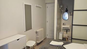 Una habitación de hotel moderna con cama, escritorio, silla, radiador, espejo y una ventana pequeña.