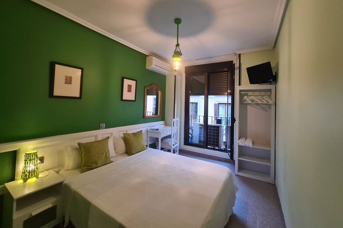 A bedroom with a bed, bedside tables, a wardrobe, a mirror, and a view of the outside.