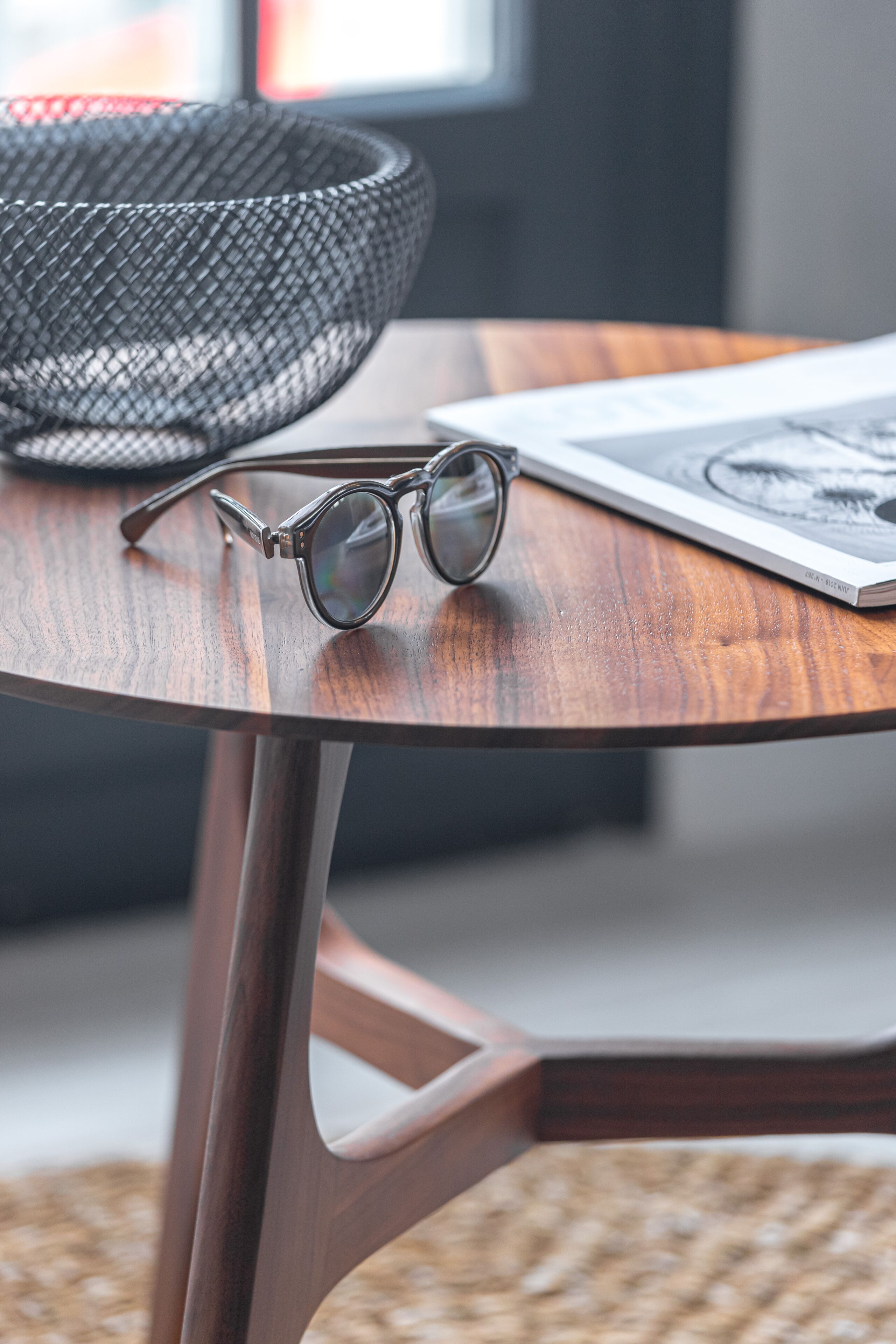 A round wooden table with a pair of glasses and a magazine.