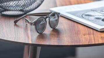A round wooden table with a pair of glasses and a magazine.