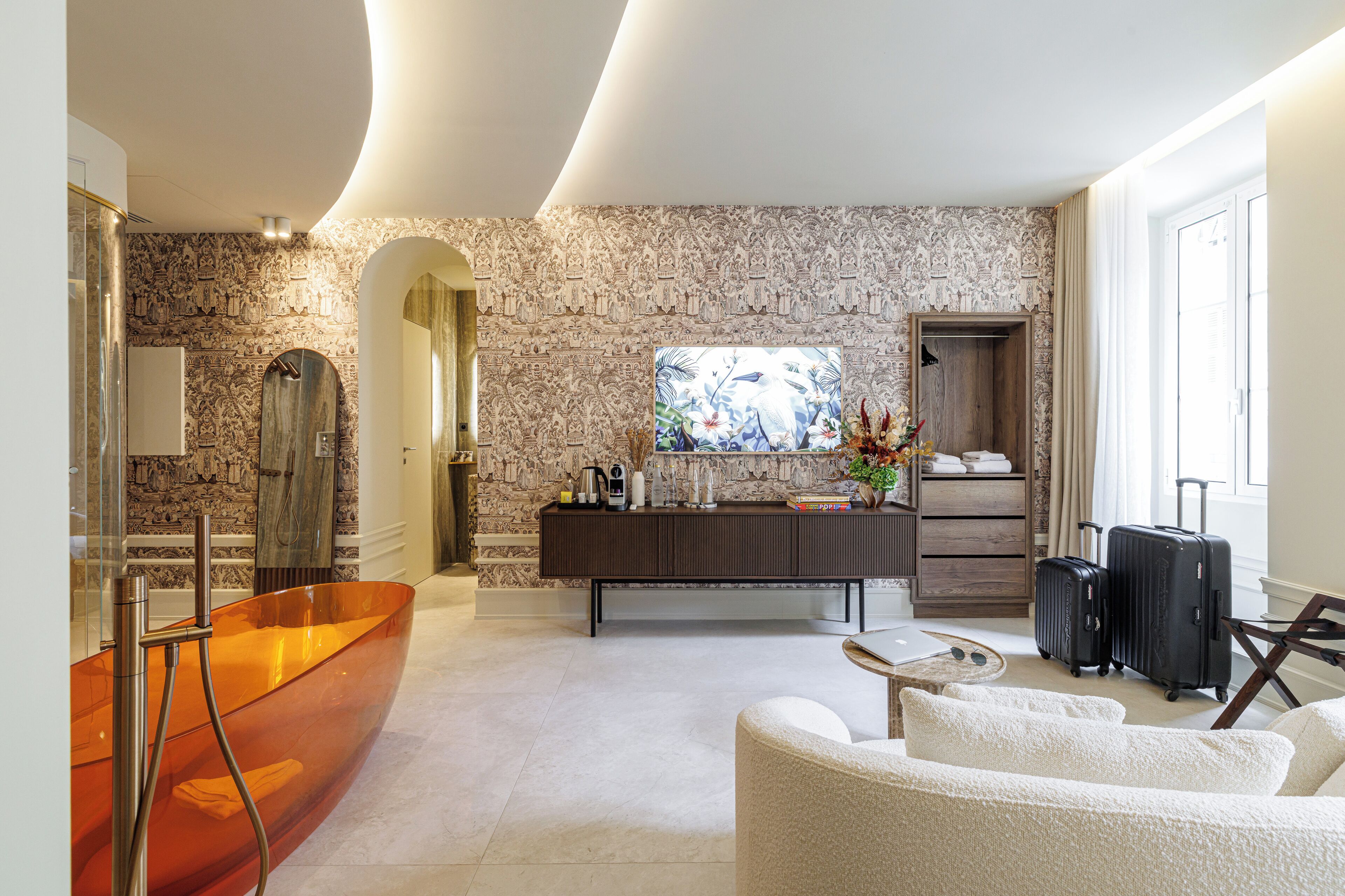 A modern bathroom with a large glass bathtub, a vanity with a mirror, and a shower area. There is a seating area with a white sofa and a coffee table.