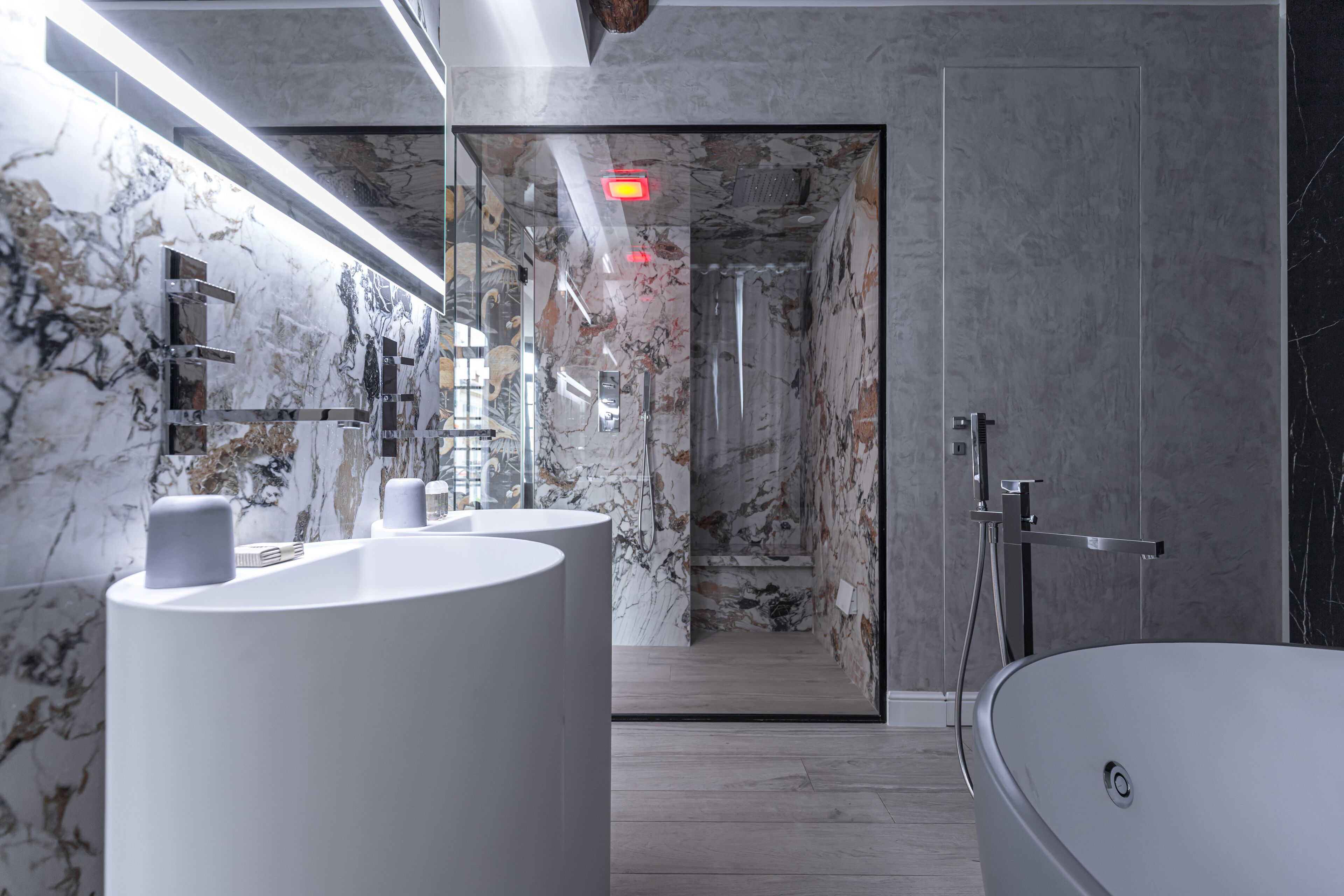 A modern bathroom with a marble wall, a large bathtub, and a glass shower enclosure.