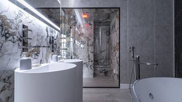 A modern bathroom with a marble wall, a large bathtub, and a glass shower enclosure.