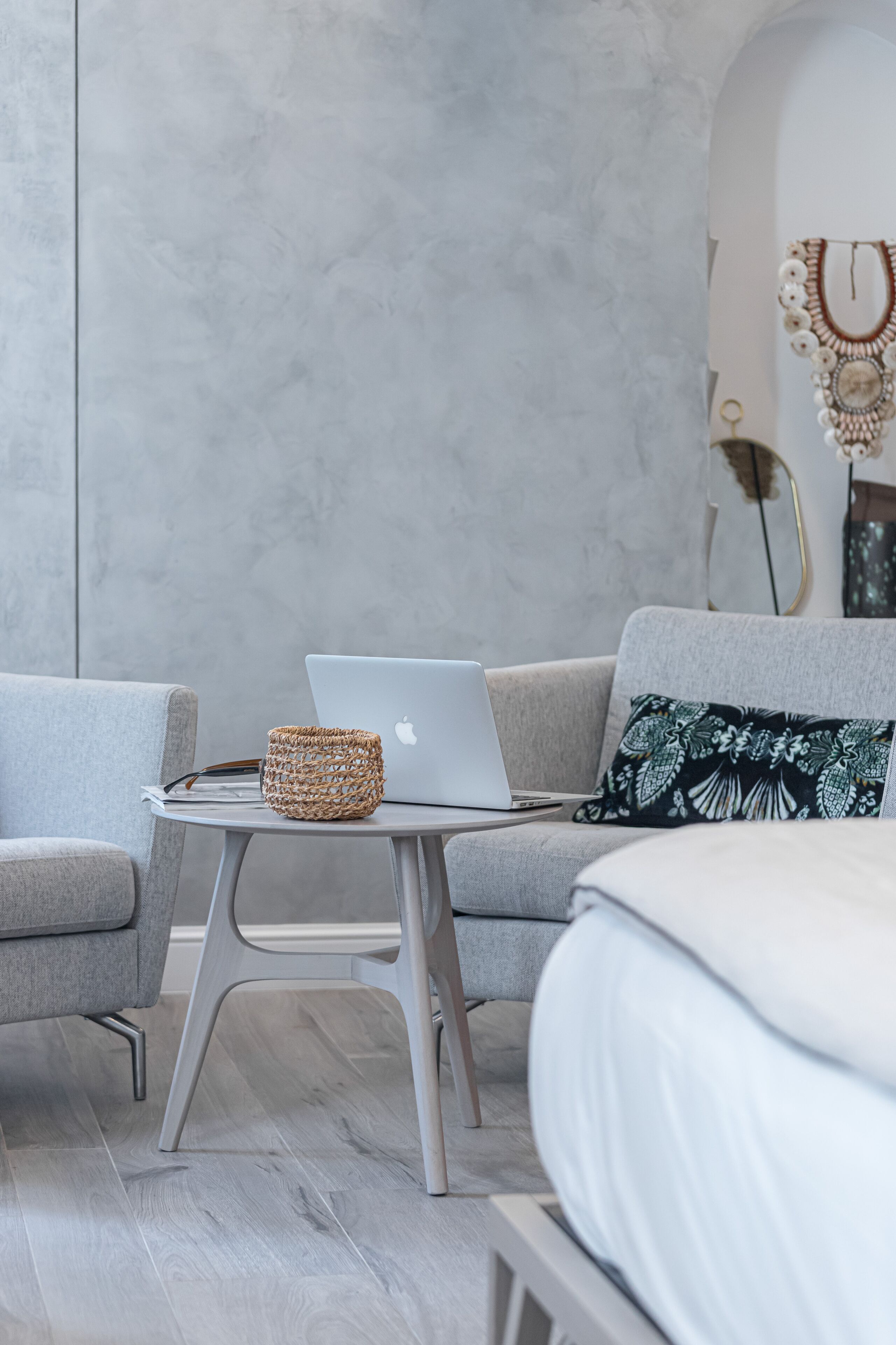 A modern room with a grey sofa, a small round table with a laptop, and a woven basket.