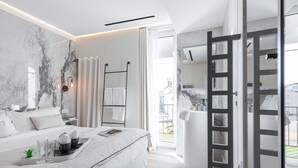 A modern hotel room with a large bed, a bedside table with a tray, a large mirror, and a view of the city through the window. - Le Dortoir Boutique Suites (Nice)