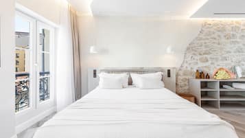 Un dormitorio moderno con una cama grande, una pared de acento de piedra y un balcón con vistas a edificios.