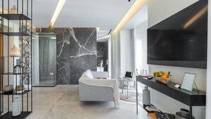 A modern living room with a grey sofa, a black TV mounted on the wall, and a glass coffee table. - Le Dortoir Boutique Suites (Nice)
