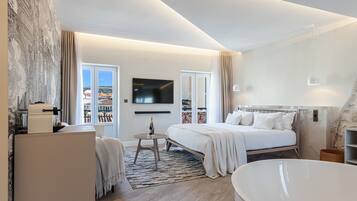 Una camera d'albergo moderna con un letto grande, una zona salotto con un tavolino, una TV a schermo piatto montata a parete e vista sulla città dalle finestre.
