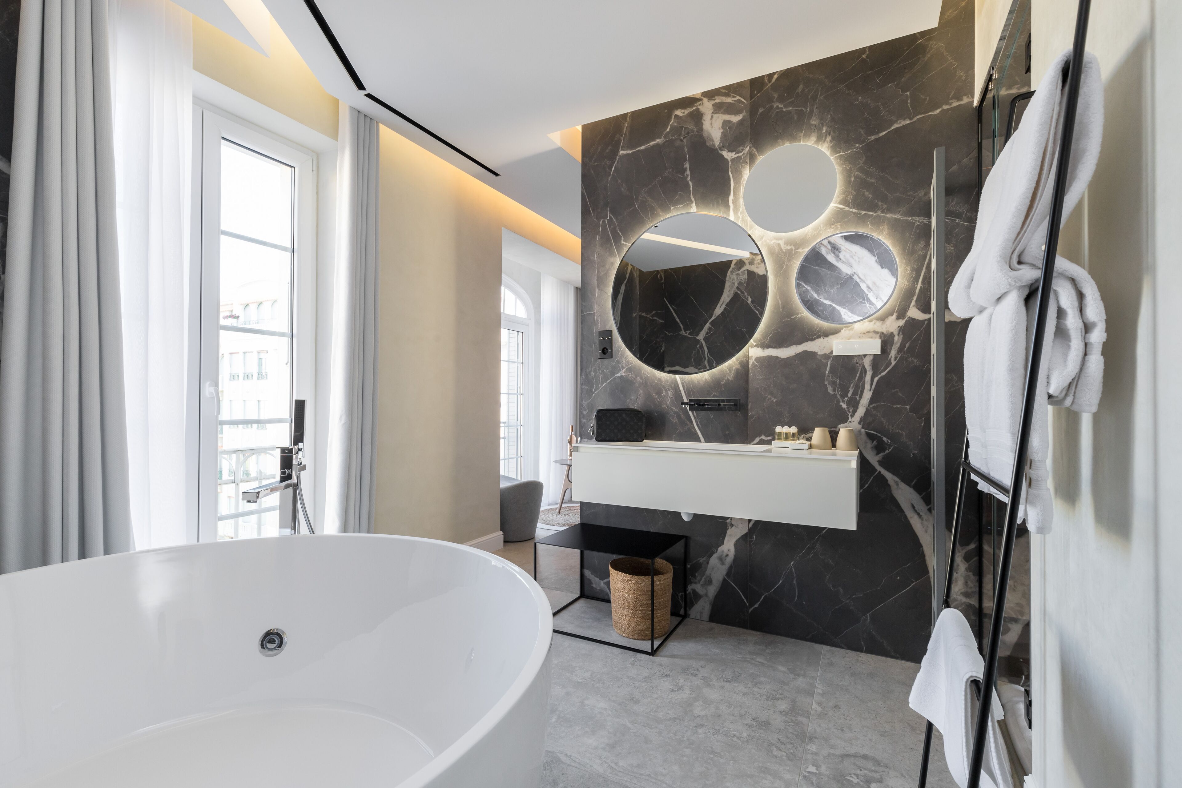 Un baño moderno con una bañera independiente, un tocador de mármol y un espejo grande con detalles circulares.