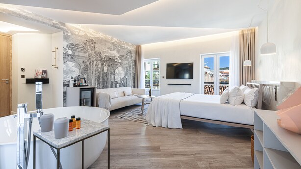 A modern hotel room with a large bed, a sofa, a small table, and a bathtub. - Le Dortoir Boutique Suites (Nice)