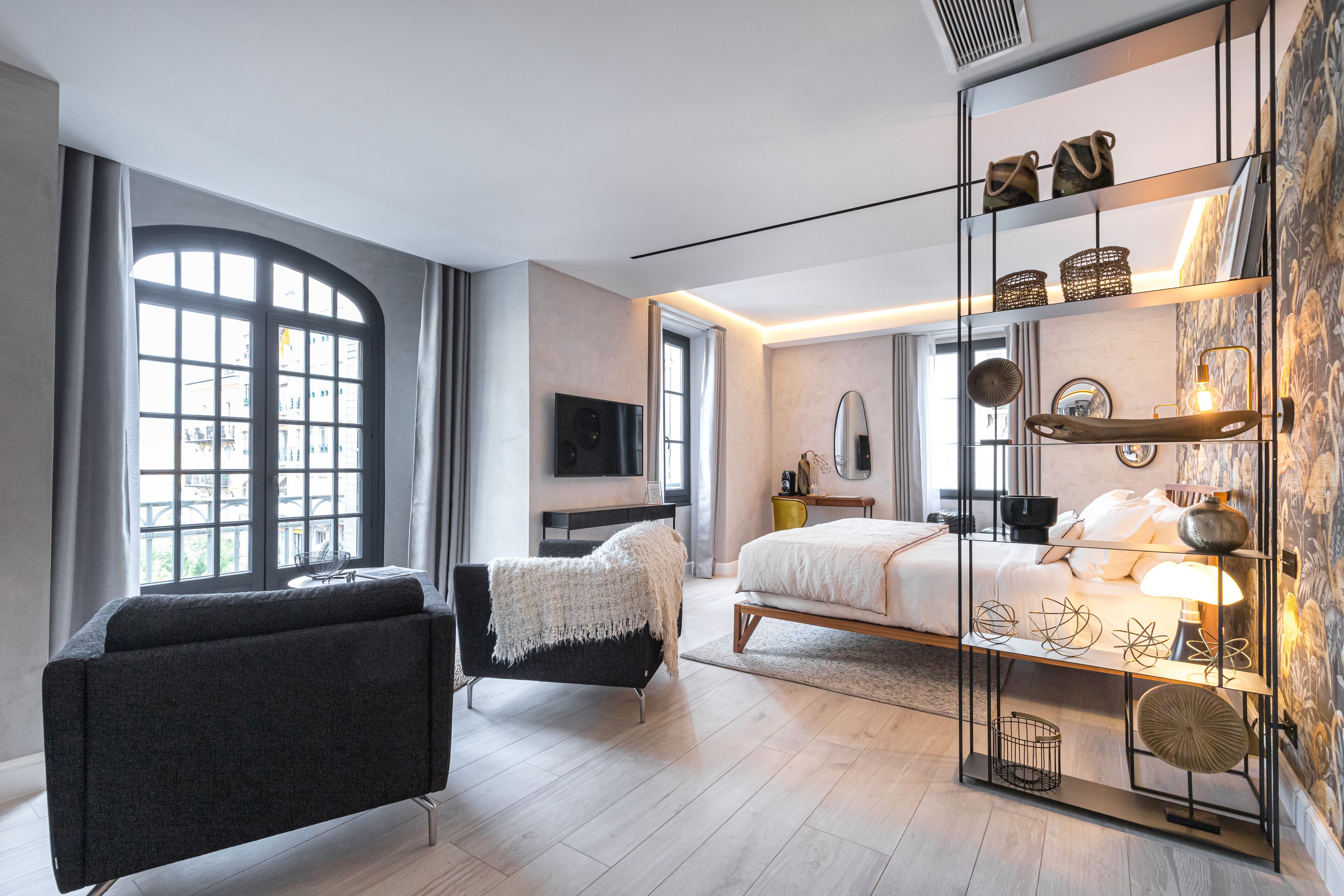 A modern bedroom with a large window, a sofa, a bed, and a bedside table with decorative items.