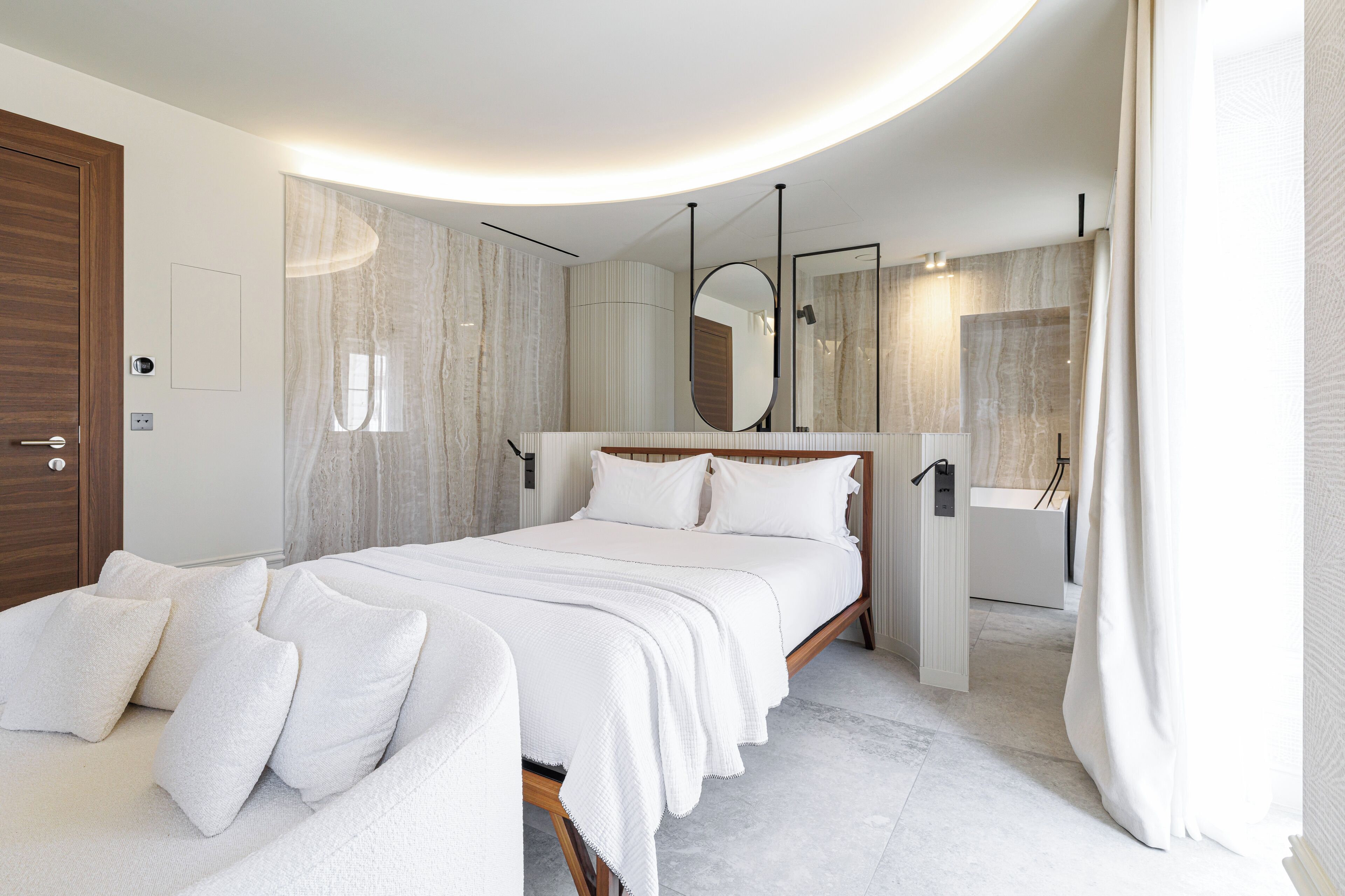 Une chambre moderne avec un grand lit, une table de chevet, un miroir et une salle de bain avec une baignoire.