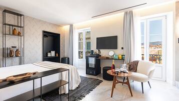 A modern hotel room with a bed, a desk, a chair, a TV, and a view of the city.
