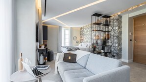 A modern living room with a grey sofa, a small round table with a laptop and a bottle, and a decorative wall with a floral pattern. - Le Dortoir Boutique Suites (Nice)