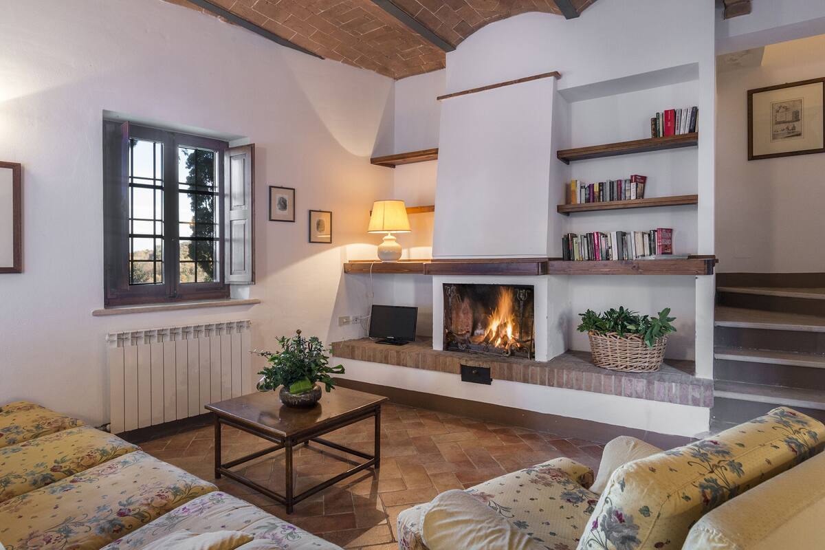 A cozy living room with a fireplace, a sofa set, a coffee table, and a bookshelf.
