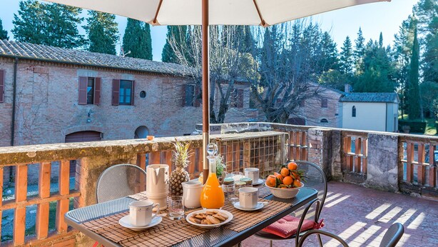 A balcony with a table set for breakfast, including a bowl of oranges, a pineapple, and various breakfast items. - Tenuta la Campana (Asciano)