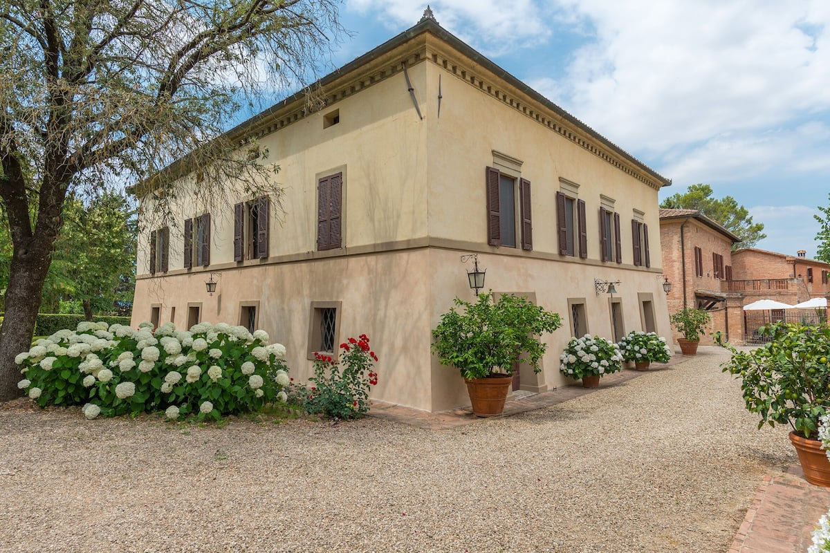 A two-story building with a symmetrical facade, multiple windows with shutters, and a gravel courtyard.