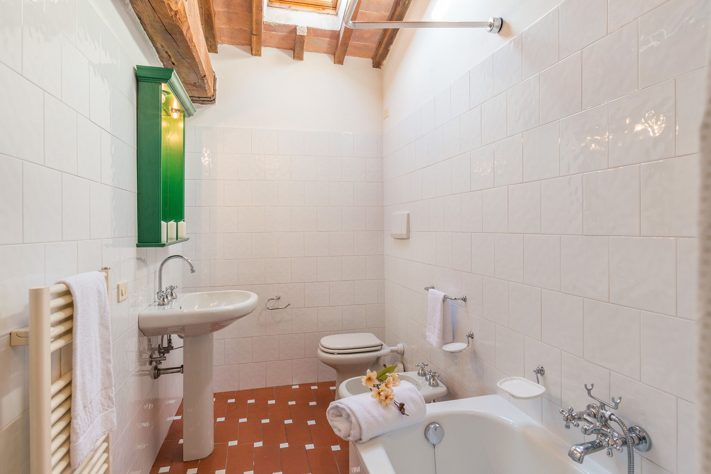 A bathroom with a white sink, toilet, and bathtub, a towel rack, and a green mirror.