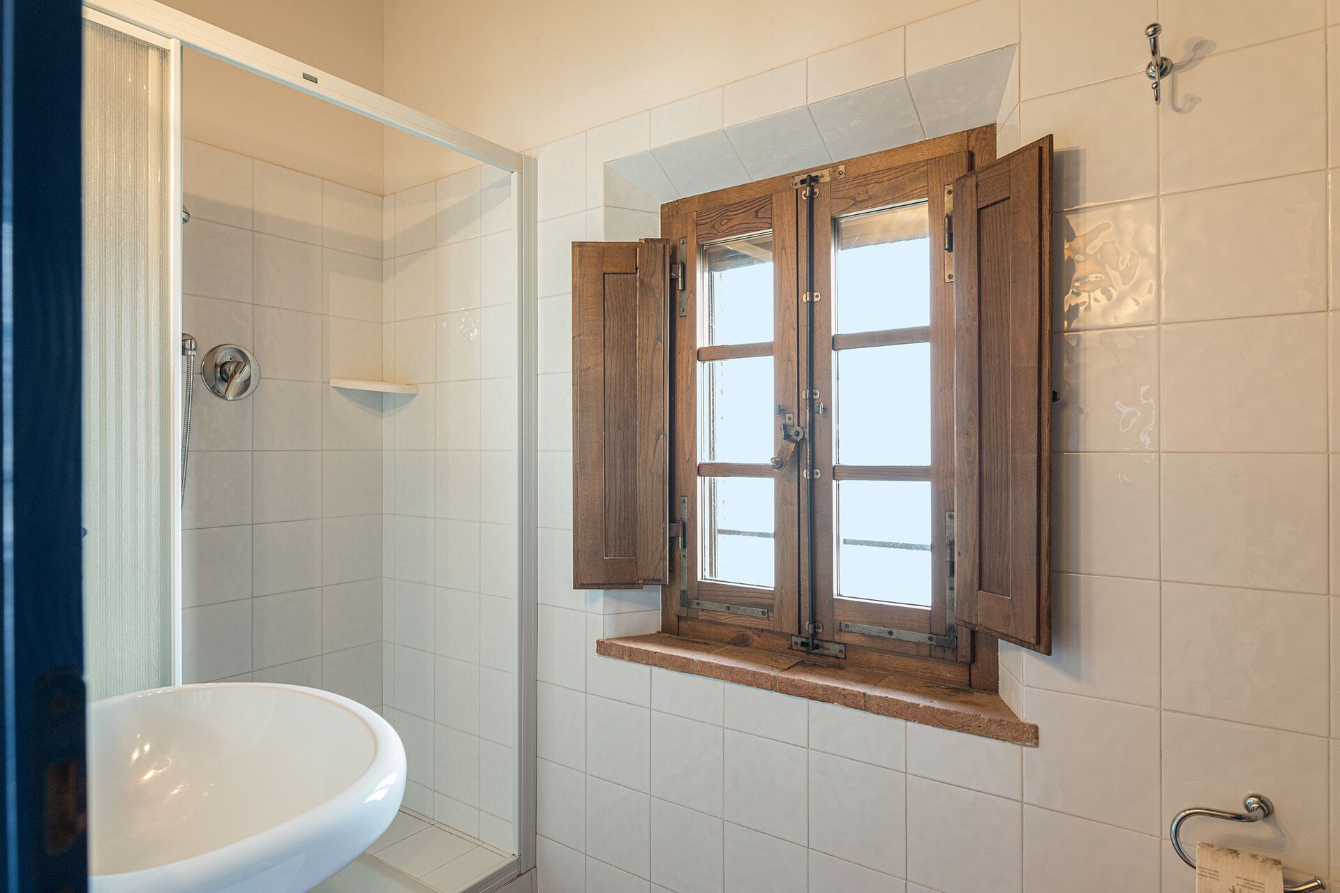 A bathroom with a shower, a toilet, and a window with wooden shutters.