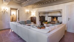 A living room with a large beige sofa, a fireplace, and exposed wooden beams on the ceiling. - Tenuta la Campana (Asciano)