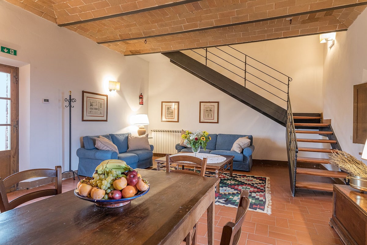 A cozy living room with a wooden table, blue sofas, and a staircase.