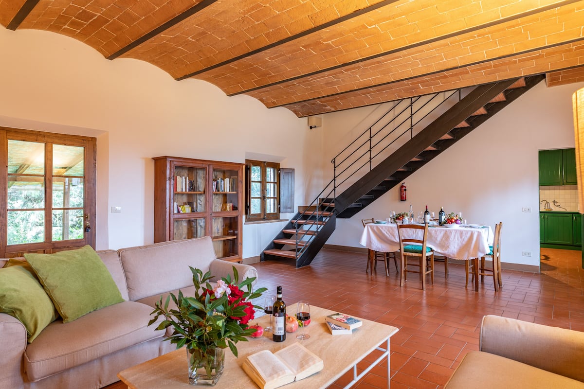 A spacious living area with a sofa, a coffee table with books and a vase, a staircase, and a dining area with chairs and a table.