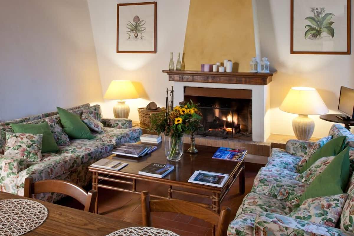 A cozy living room with floral-patterned sofas, a wooden coffee table, and a fireplace.