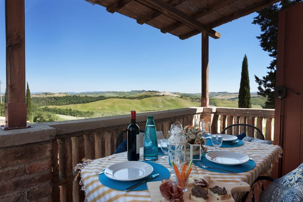 A table set for two with a view of rolling hills, a bottle of wine, and a glass of water.