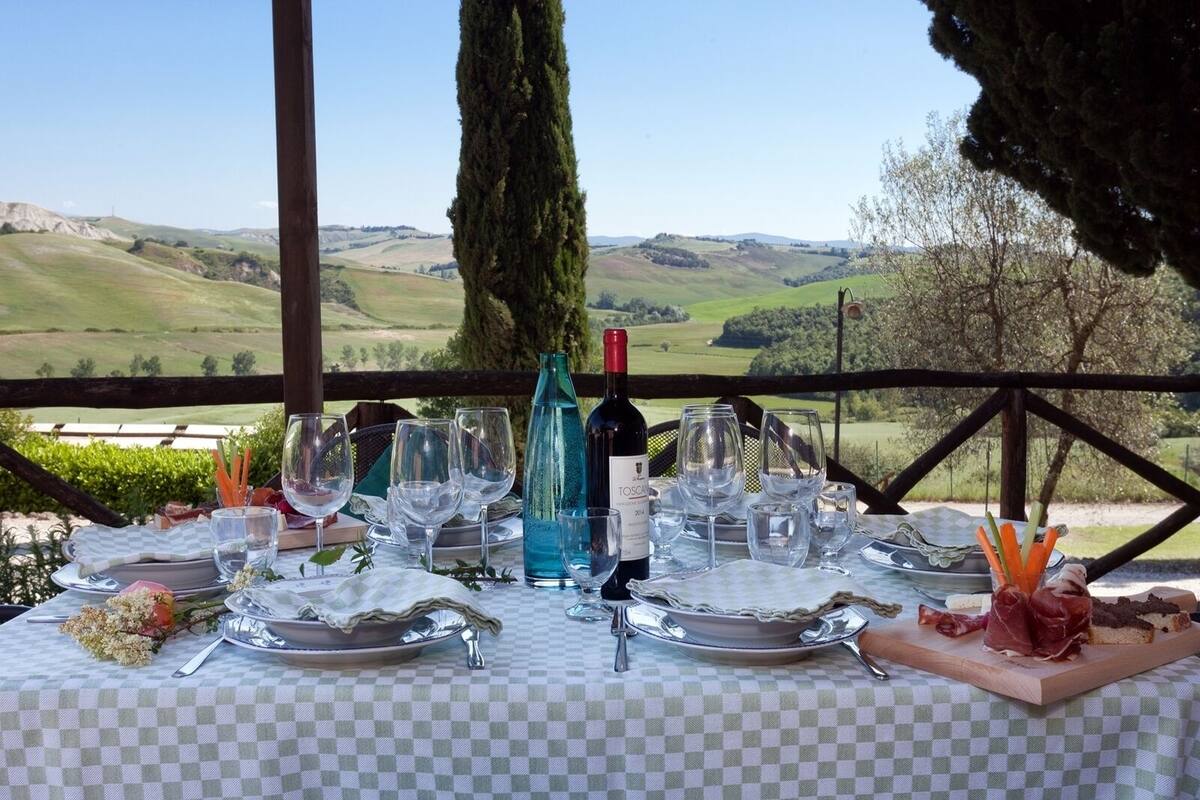 A table set for a meal with a scenic view of rolling hills and a tall tree in the background.