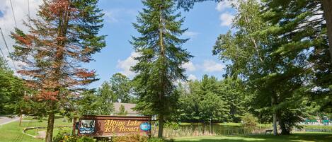 Een bord voor Alpine Lake RV Resort, omringd door bomen en een gazon.