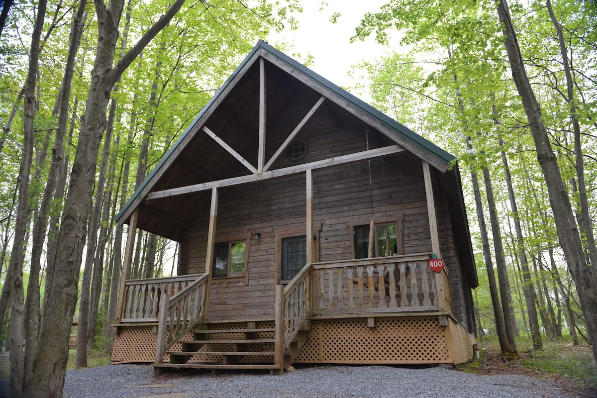 A wooden cabin with a porch and steps, surrounded by trees.