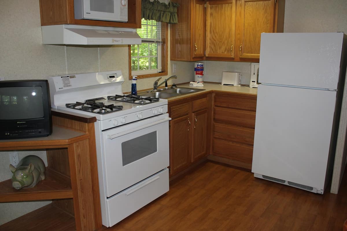 A compact kitchen with wooden cabinets, a white stove, a refrigerator, and a small television on a wooden shelf.