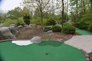 A miniature golf course with a green putting area, sand traps, and a wooded backdrop. - Appalachian Campsites (Hamburg)