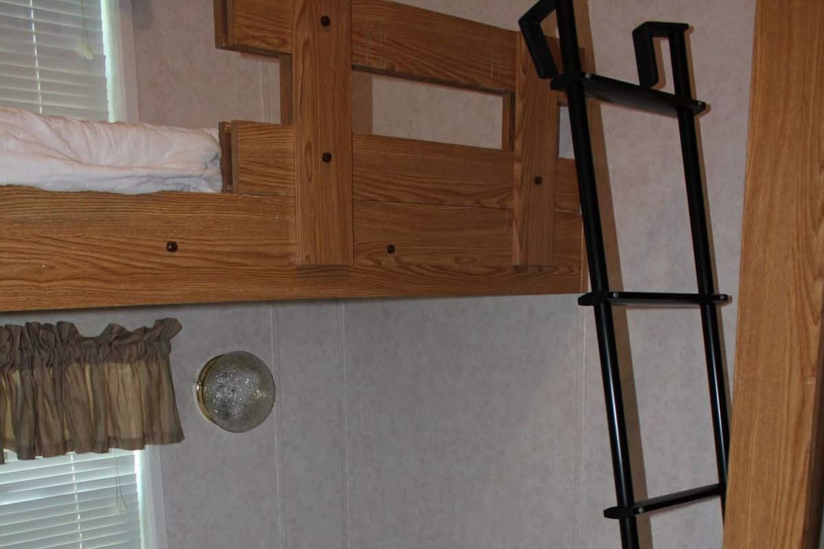 A bunk bed with a ladder, a window with blinds, and a door.