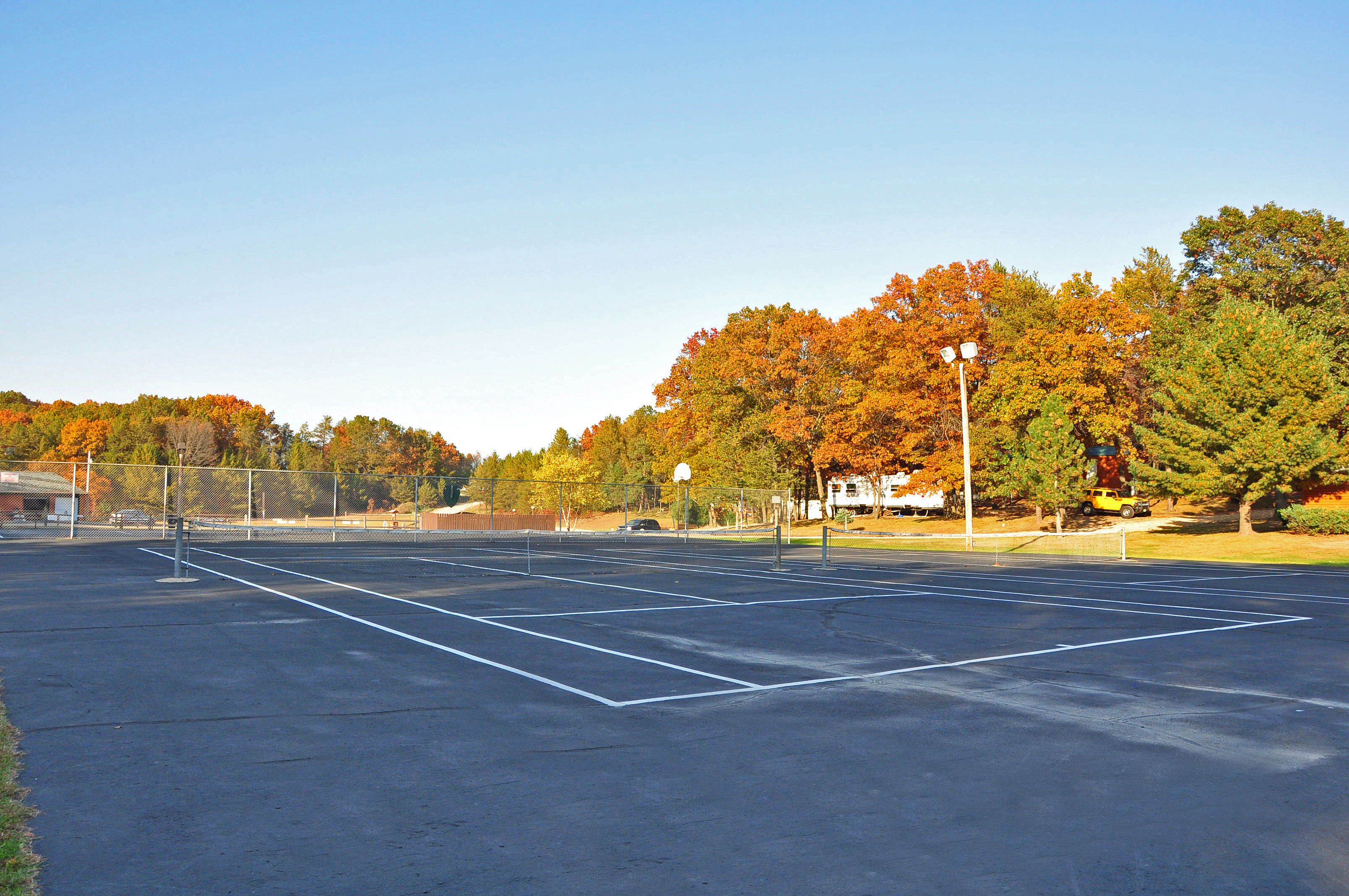 An outdoor tennis court with a clear sky, surrounded by trees with autumn foliage.